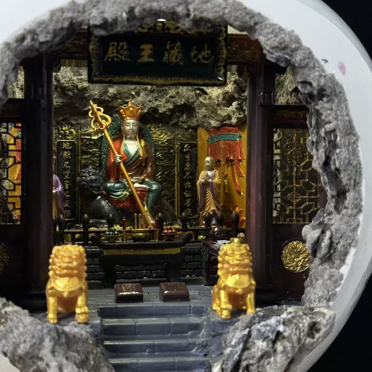 Close-up interior view of the 地藏王殿 miniature shrine diorama featuring Ksitigarbha Bodhisattva seated on a throne holding a golden ringed staff, flanked by two attendant figurines and two gold Kirin guardians on the altar steps, with dark carved wooden panels and the 地藏王殿 plaque above the entrance