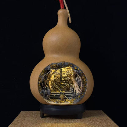 Front view of a natural double-gourd calabash vessel with an oval cave cutout on the lower bulb, revealing an illuminated miniature diorama featuring a large closed door with gold Buddha face glowing inside a cave with gnarled tree roots, with a small Sun Wukong figurine at the base, displayed on a black round stand on a burlap mat against a black background