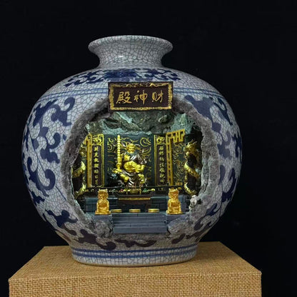 A porcelain vase with a blue and white crackled glaze, featuring a carved opening that reveals an ornate miniature golden Wu Caishen golden temple inside. The vase is displayed on a textured beige pedestal against a solid black background.