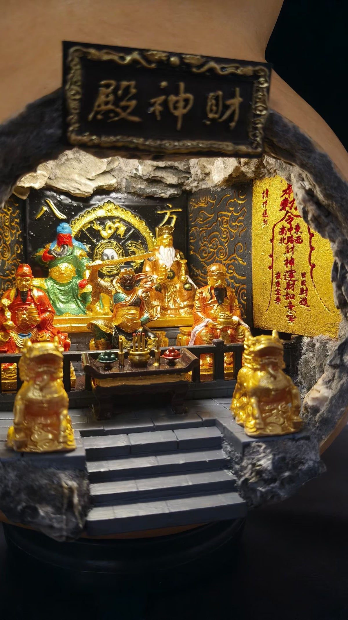 Close-up front view of a miniature Five Roads God of Wealth shrine diorama (财神殿), showing five gold and colorful deity figurines seated in a row with gold pixiu guardians on the steps and a golden blessing scroll on the right wall