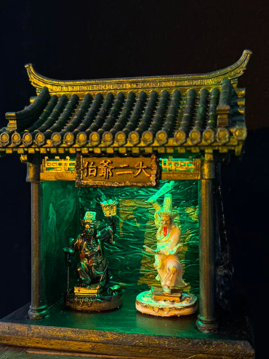 Front view of a miniature car shrine temple model featuring Tua Di Ya Pek figurines under green lighting, against a black background