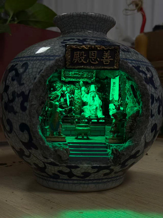 Alternate angle of a blue and white porcelain vase with an illuminated Tua Di Ya Pek shrine diorama inside, showing the decorative exterior and glowing interior detail