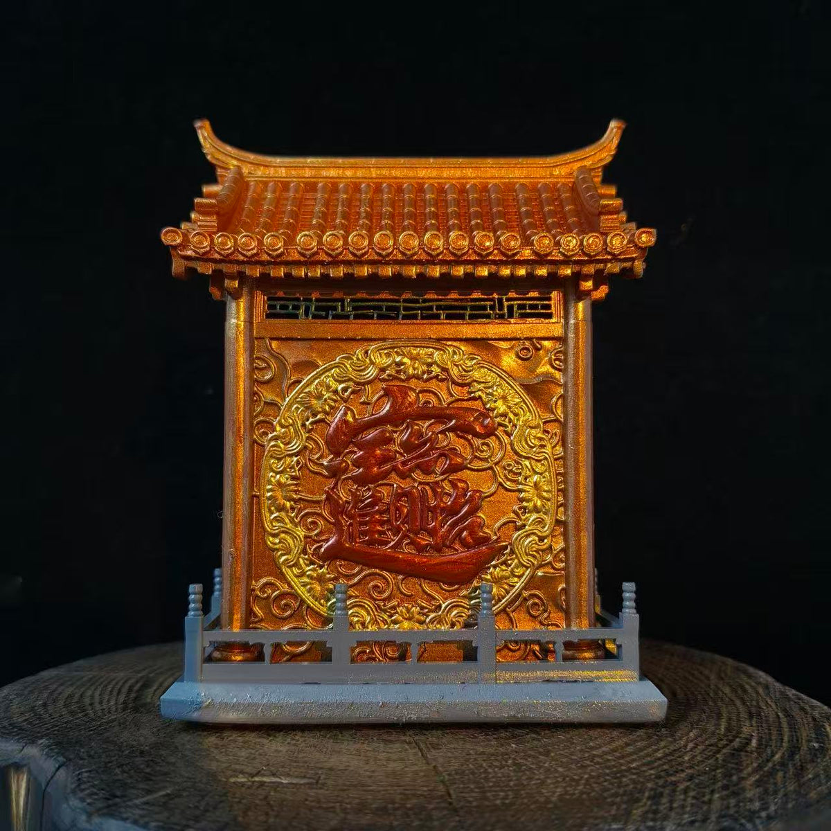 Rear view of a custom miniature shrine model displayed on a wooden log base against a black background, showing a large gold embossed Chinese character in a circular cloud motif on the back panel with a pagoda roof above and grey balustrade fence below