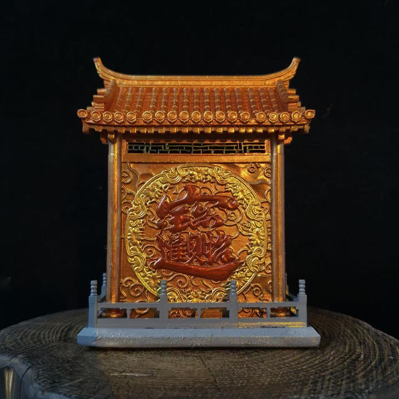 Rear view of a custom miniature shrine model displayed on a wooden log base against a black background, showing a large gold embossed Chinese character in a circular cloud motif on the back panel with a pagoda roof above and grey balustrade fence below