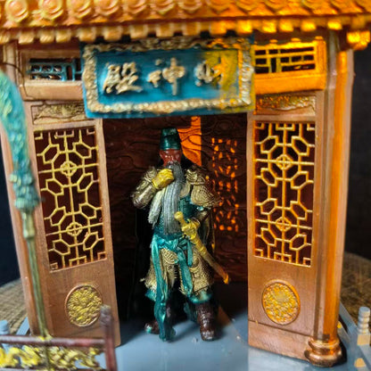 Close-up front view of a custom miniature shrine model featuring a Guan Yu figurine in golden-green armour standing in the doorway, with gold lattice side panels and a teal plaque reading 财神殿 above the entrance