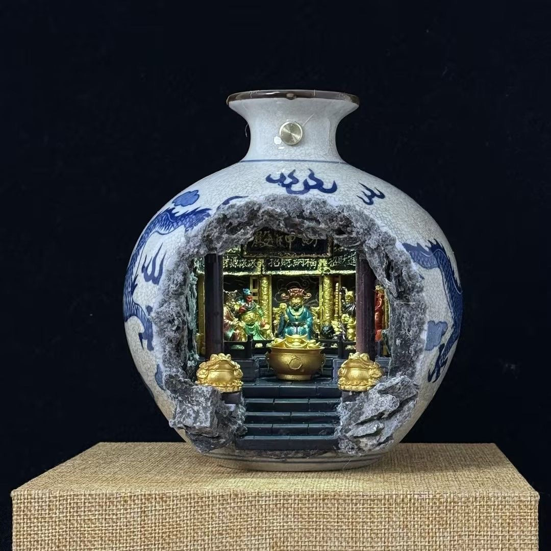 A blue and white porcelain vase with a cutout front revealing an illuminated miniature shrine diorama of Five Roads God of Wealth, displayed on a burlap mat against a black background
