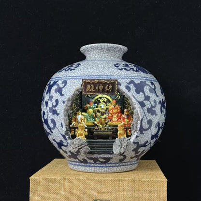Blue and white crackle-glaze porcelain vase with a cave cutout revealing an illuminated Five Roads God of Wealth shrine diorama (财神殿) inside, displayed on a burlap mat against a black background