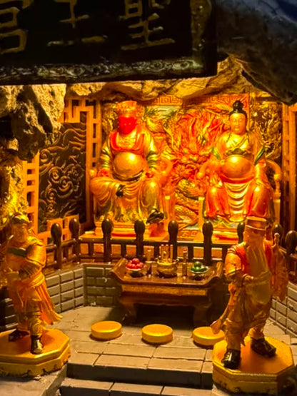 Close-up interior of the 圣王宫 miniature shrine diorama featuring Guangze Zunwang and Miaoyin Xianzi seated on thrones under warm golden light, flanked by two attendant figurines, with carved dragon-cloud wall panels behind